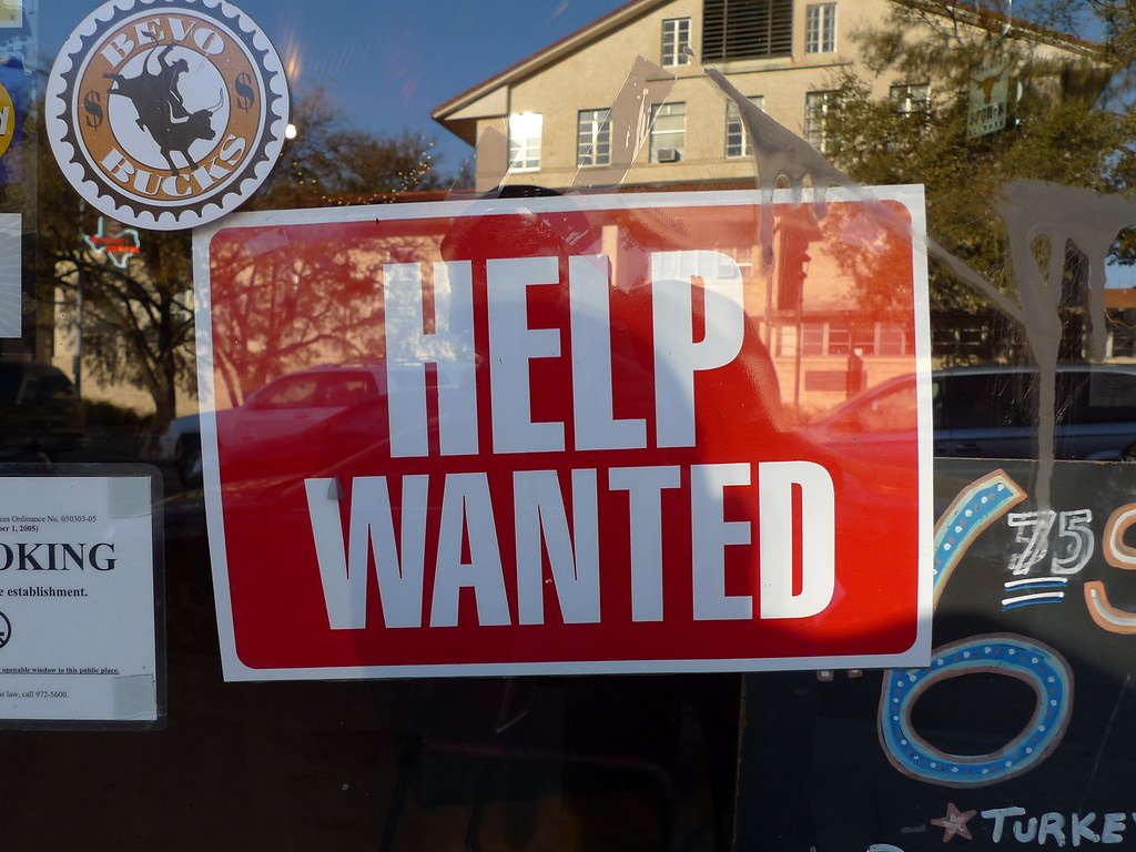 Letrero rojo con el texto en inglés Help Wanted en una vitrina