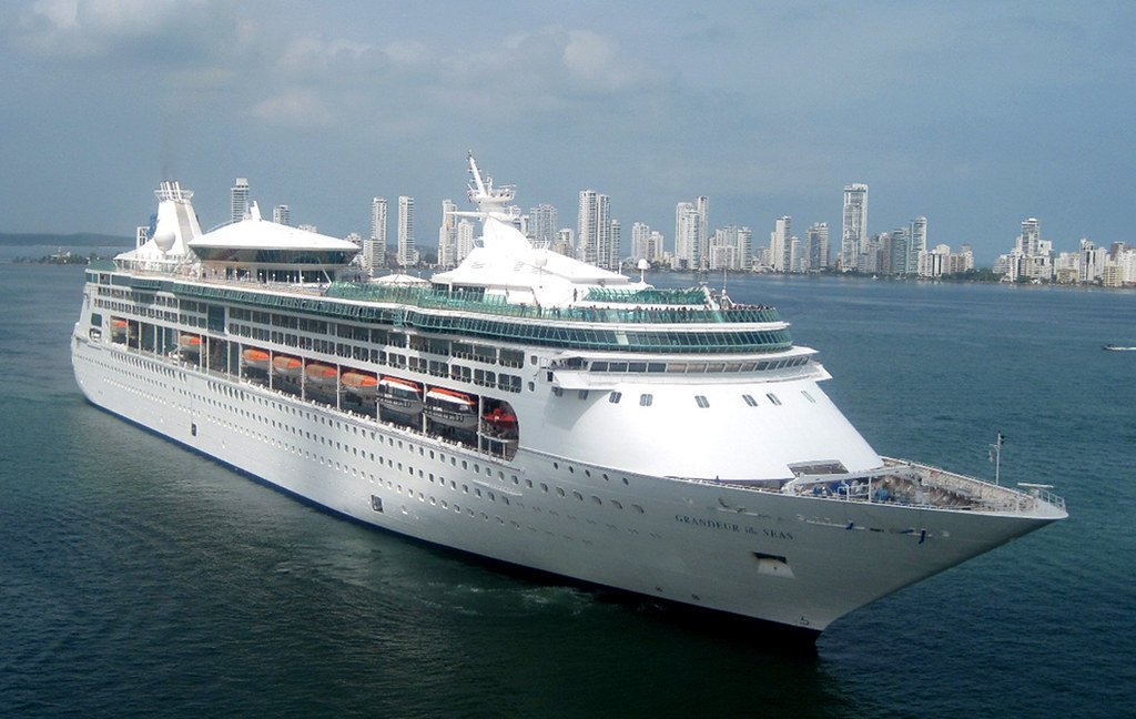 Un crucero de Royal Caribbean navegando frente a la costa de una ciudad con rascacielos.