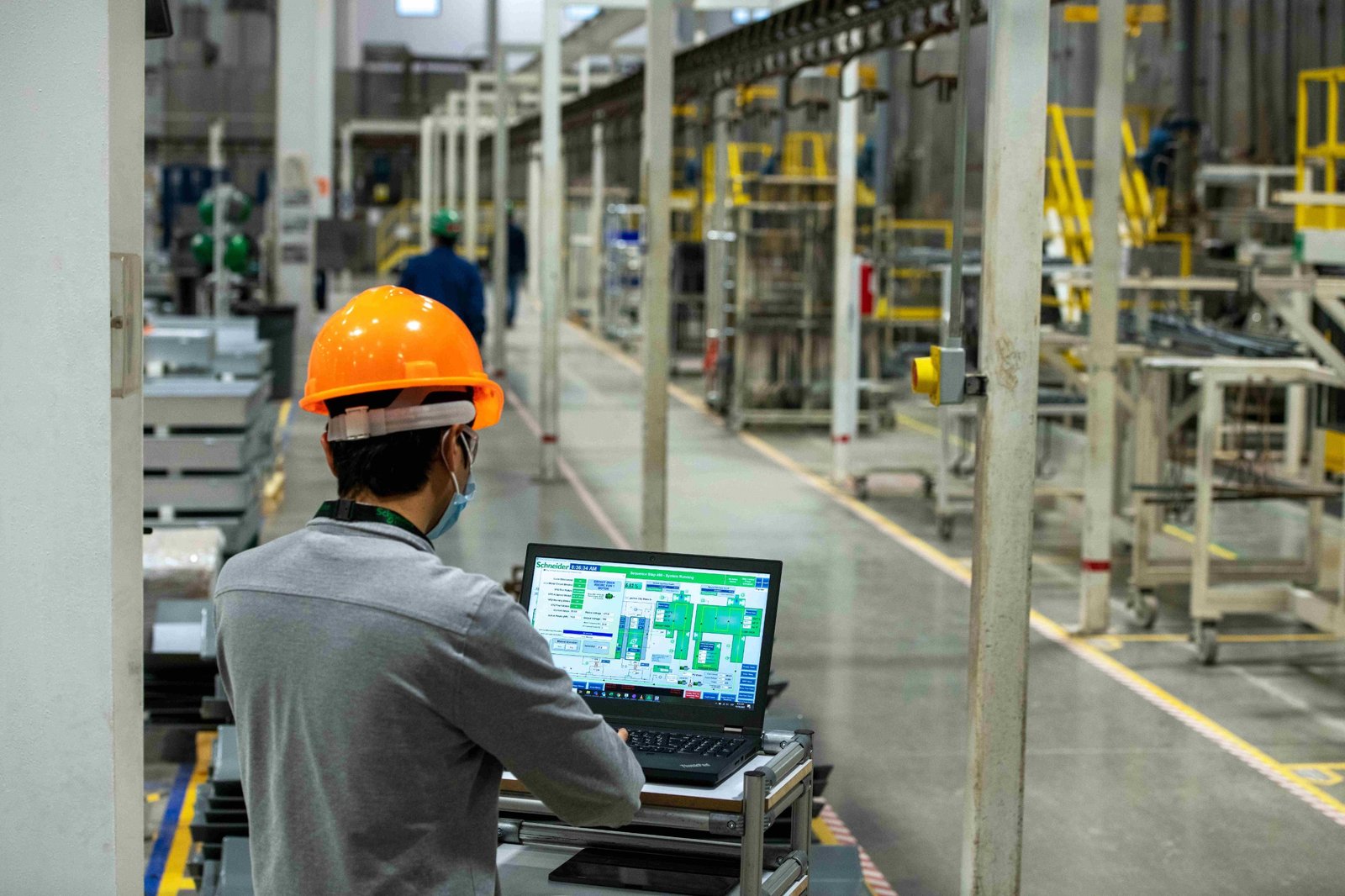 Operario con casco frente a una computadora que muestra el sistema de control de una planta industrial