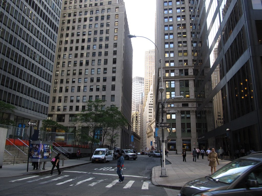 Vista de la calle Nassau en el distrito financiero de Nueva York con rascacielos, peatones cruzando la calle y vehículos.