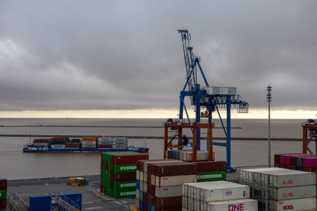 Grúas pórtico sobre contenedores apilados en una terminal portuaria, con un buque al fondo