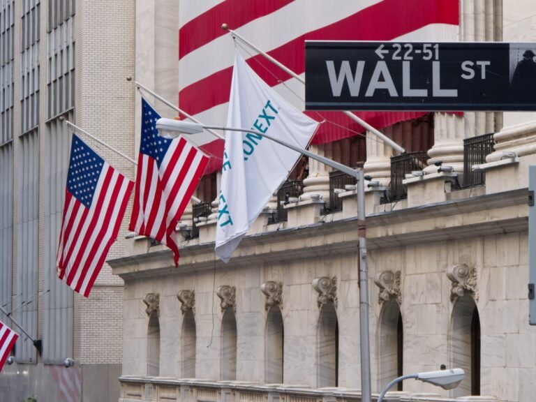Señal de Wall Street frente a la Bolsa de Nueva York y banderas estadounidenses.