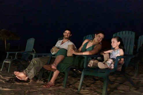 Una familia sentada en sillas de playa comparte palomitas durante una actividad nocturna.