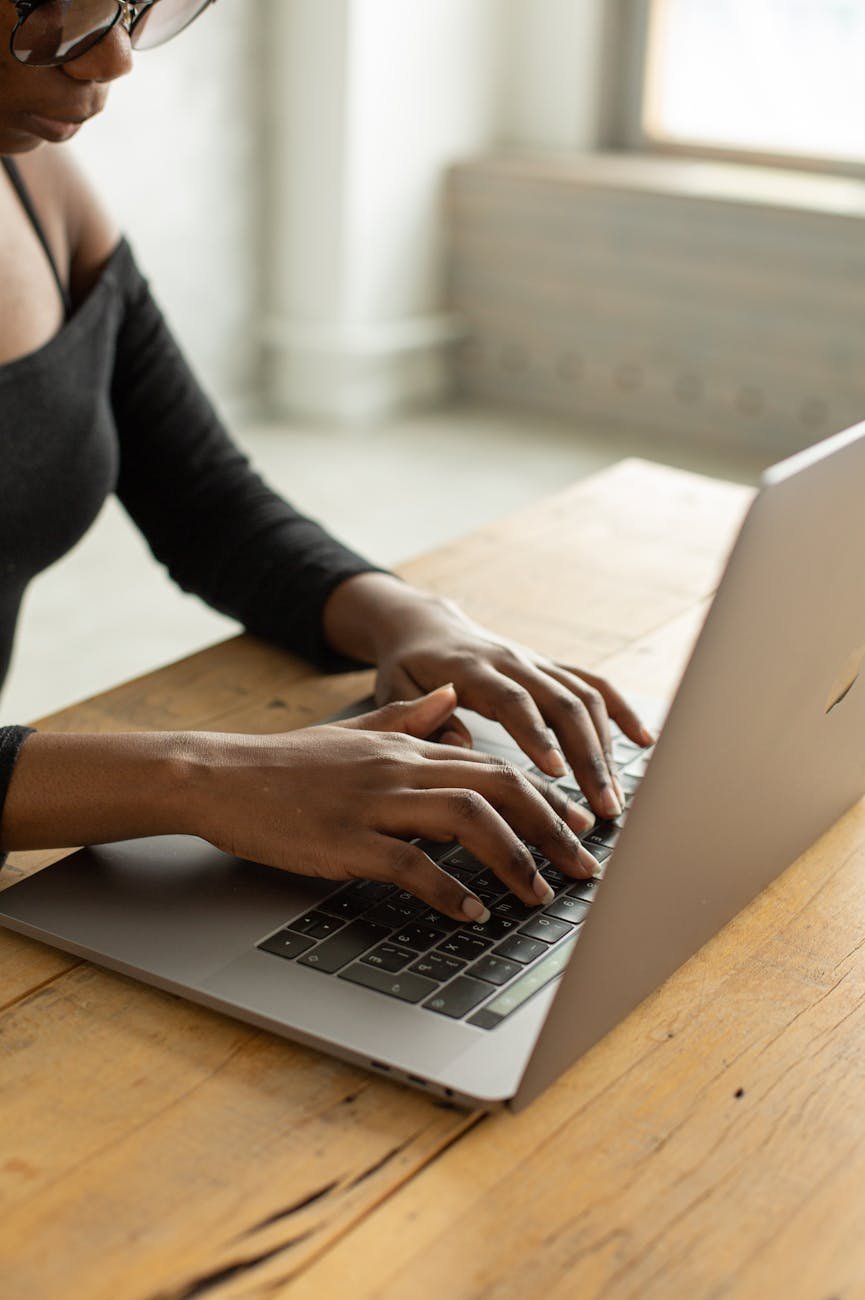 crop black woman typing on laptop in light room