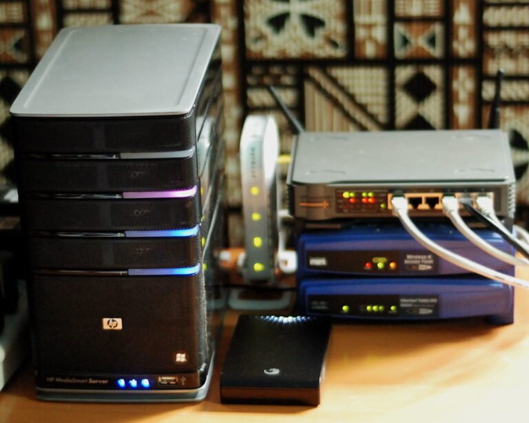 Un servidor HP MediaSmart junto a varios dispositivos de red, routers y discos duros externos conectados con cables Ethernet sobre una mesa.