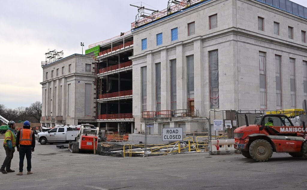 Vista exterior del edificio de la Reserva Federal Eccles en Washington D.C. durante trabajos de construcción y remodelación con maquinaria pesada y trabajadores en el sitio.