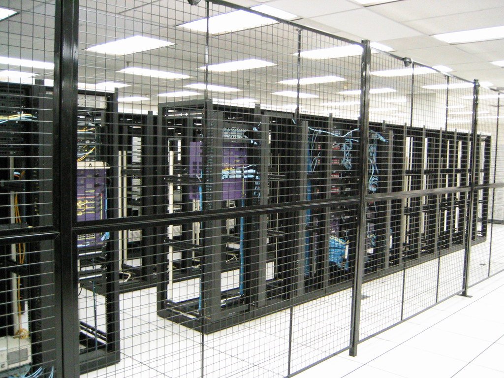 Centro de datos con filas de servidores protegidos por una jaula de seguridad metálica en una sala con suelo técnico.