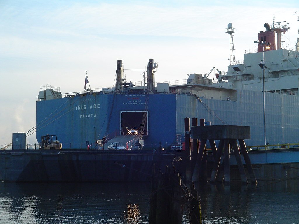 El buque carguero Iris Ace atracado en un puerto descargando vehículos a través de una rampa.