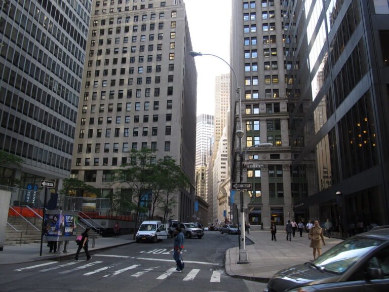 Vista de la calle Nassau en el distrito financiero de Nueva York, rodeada de grandes edificios de oficinas y rascacielos con peatones cruzando la calle.