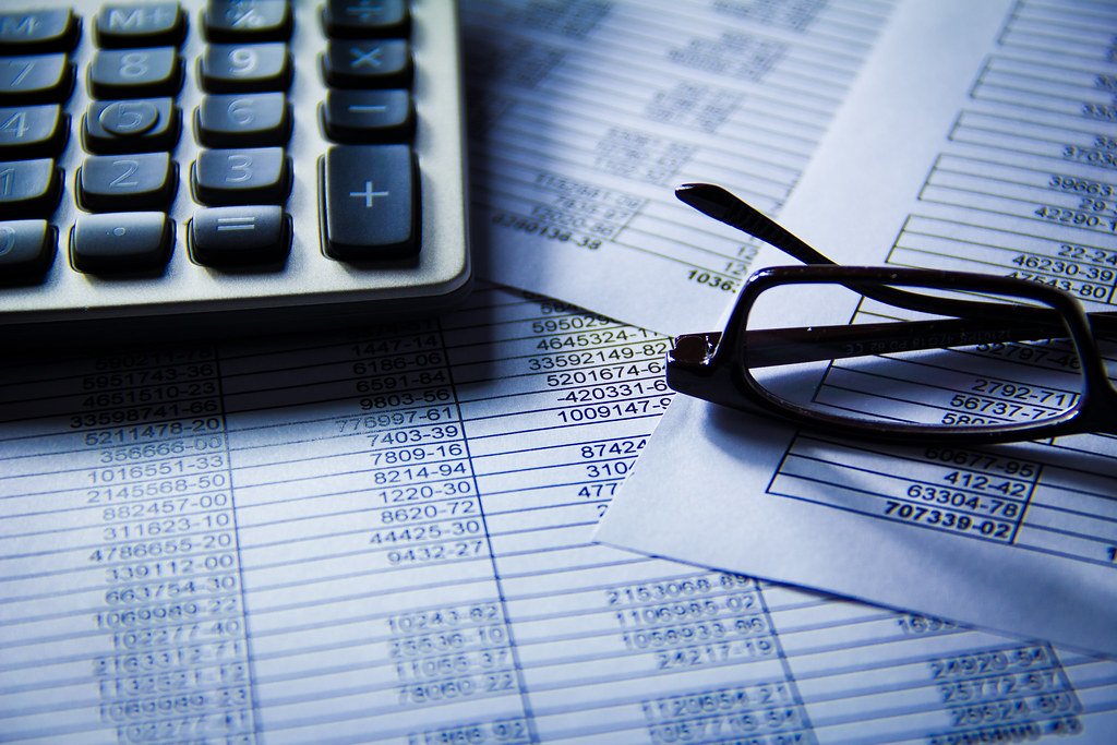 Calculadora y gafas sobre documentos con columnas de datos financieros y cifras numéricas.