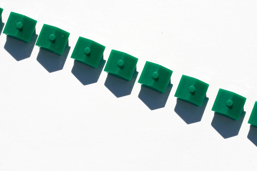 Una fila diagonal de pequeñas casas de juguete de color verde sobre un fondo blanco, proyectando sombras marcadas.