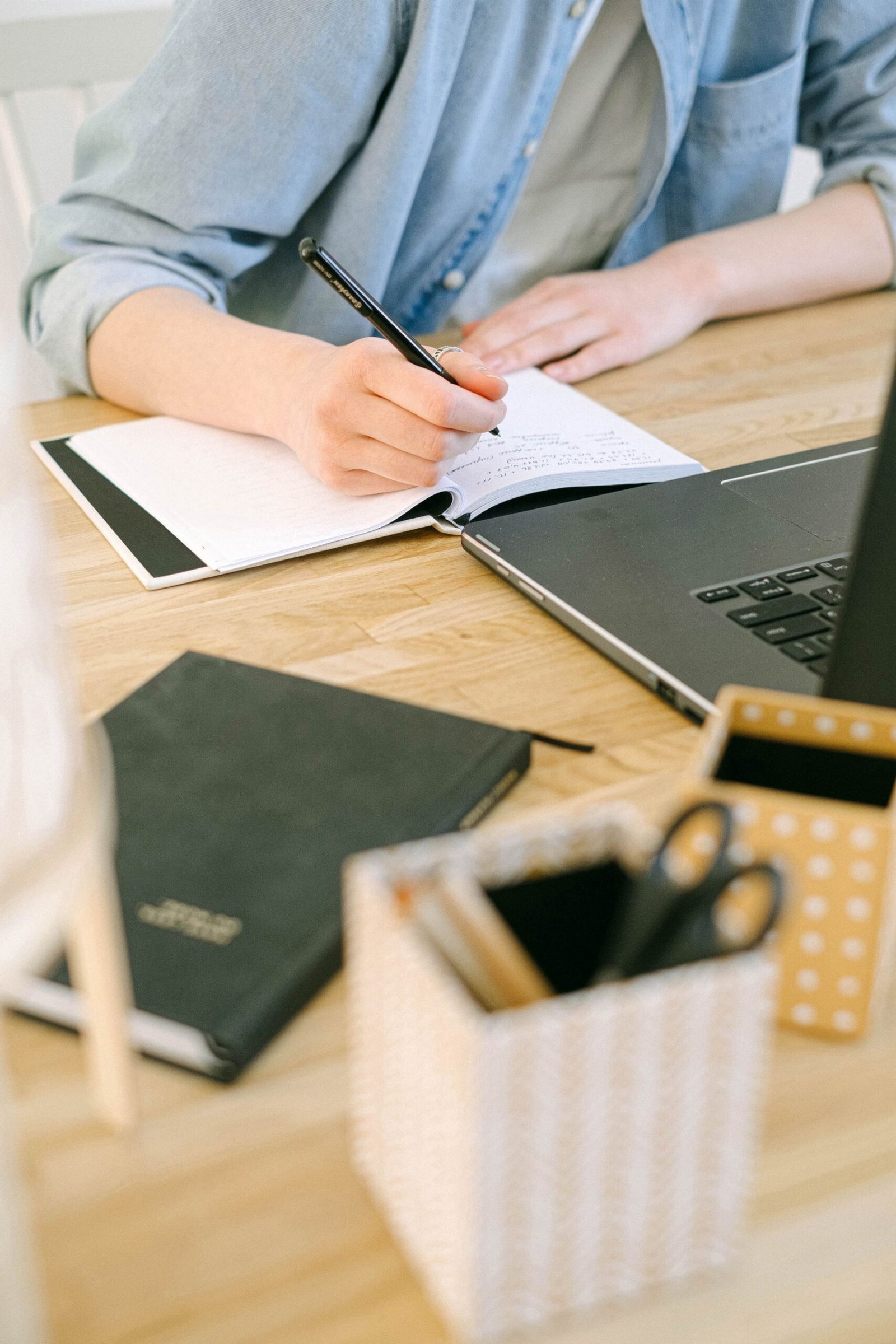 Persona escribe en un cuaderno junto a una computadora portátil