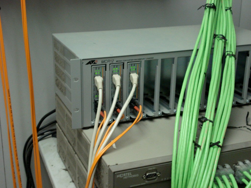 Un rack de servidores con conversores de medios y cables de red conectados en un centro de datos.